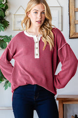 woman wearing a burgundy ribbed long sleeve top with a white button placket and relaxed fit, styled with dark jeans