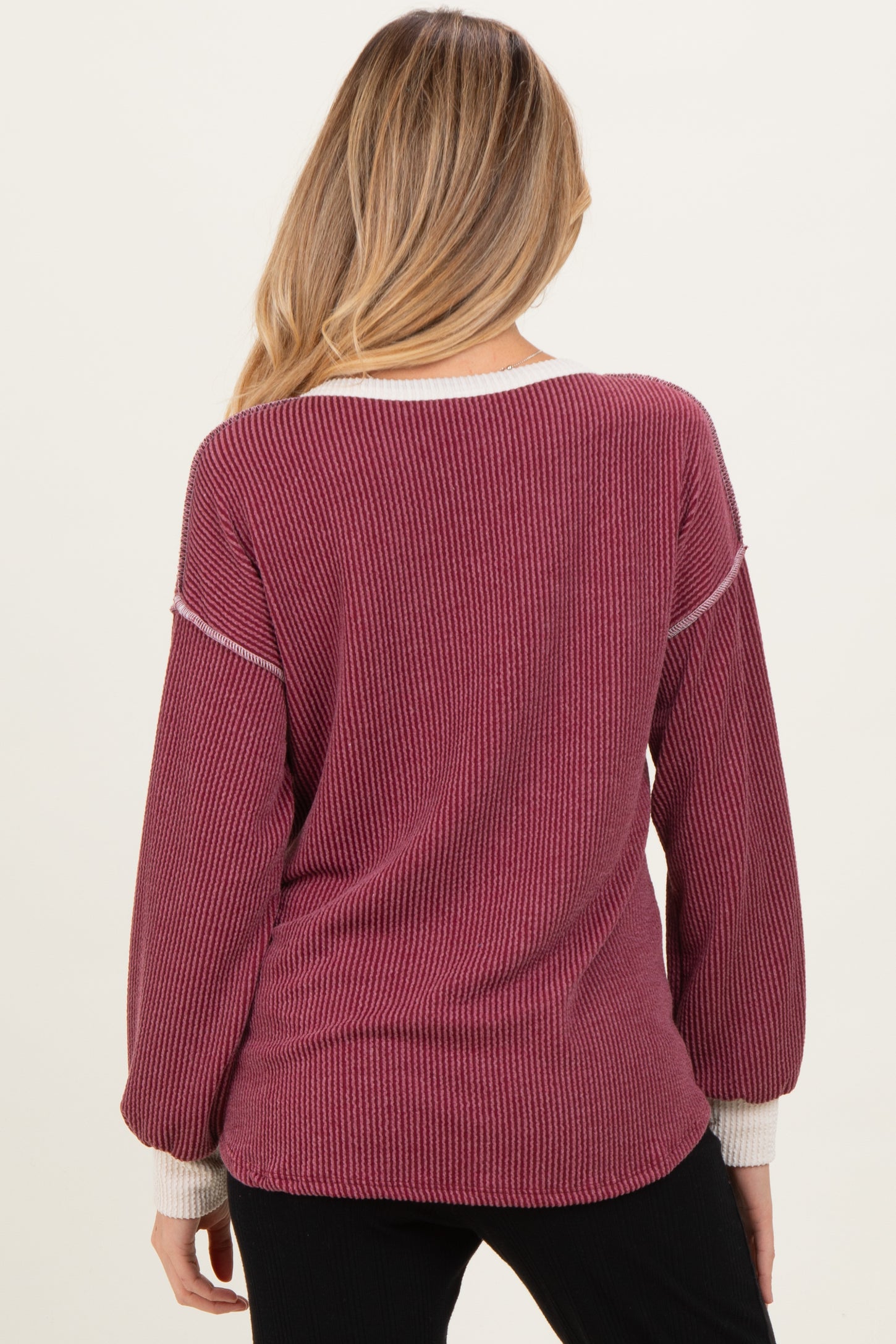 woman wearing a burgundy maternity sweater with striped details and balloon sleeves, showing the back view