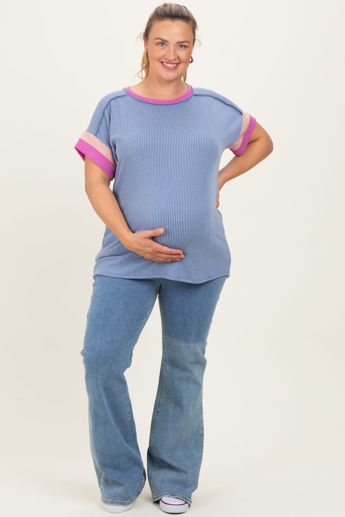 woman wearing a striped blue maternity top with pink accents and flared jeans, holding her baby bump