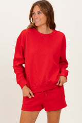 woman wearing a red oversized sweatshirt with long sleeves and a crew neckline, paired with matching shorts