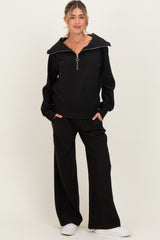 woman wearing a black maternity sweatshirt with a zip-up collar and matching wide-leg pants, styled with white sneakers