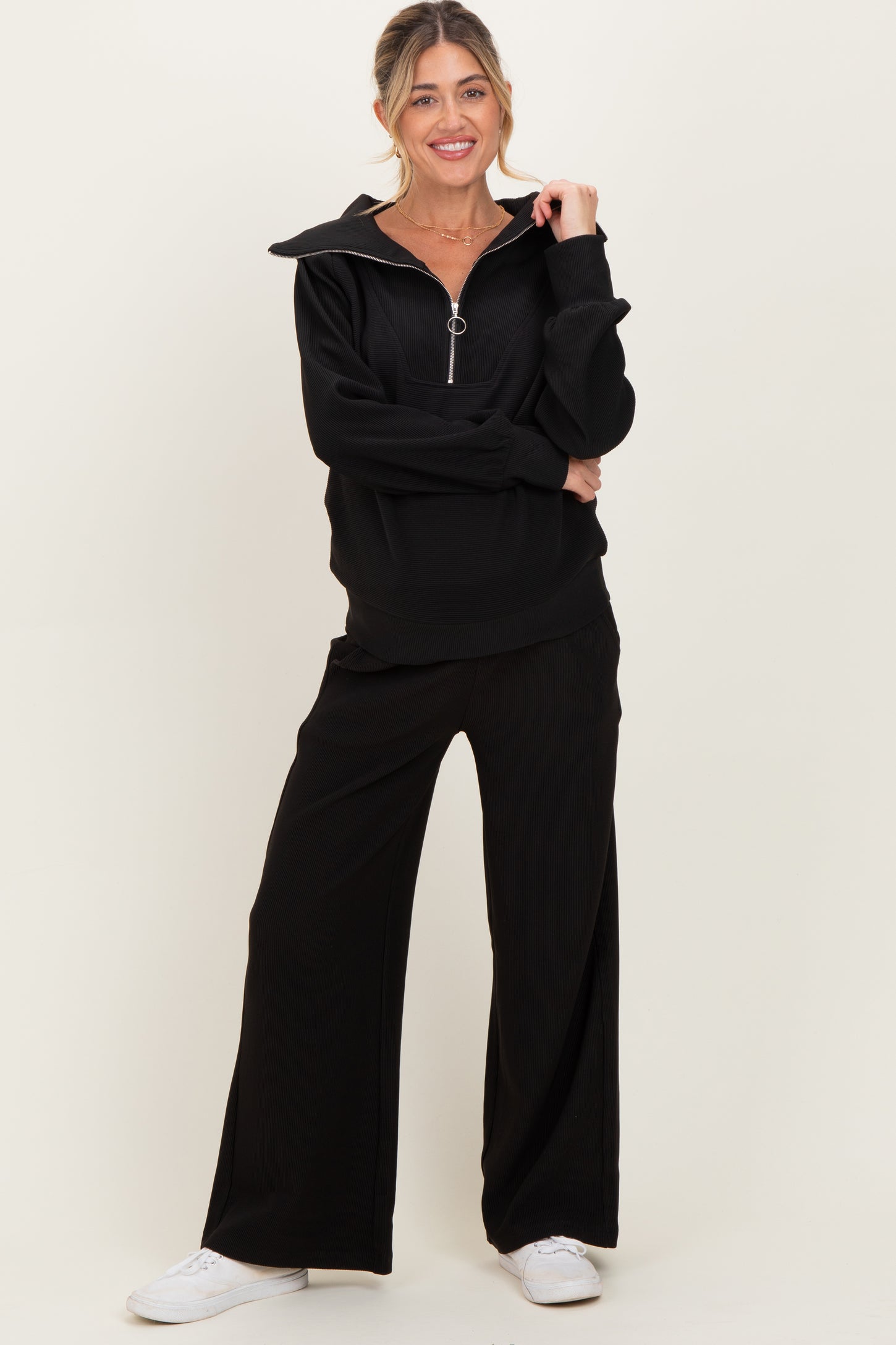 woman wearing a black maternity zip-up top with a collar and matching wide-leg pants, looking comfortable and chic