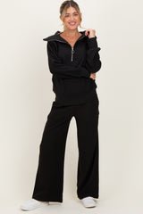 woman wearing a black maternity zip-up top with a collar and matching wide-leg pants, looking comfortable and chic