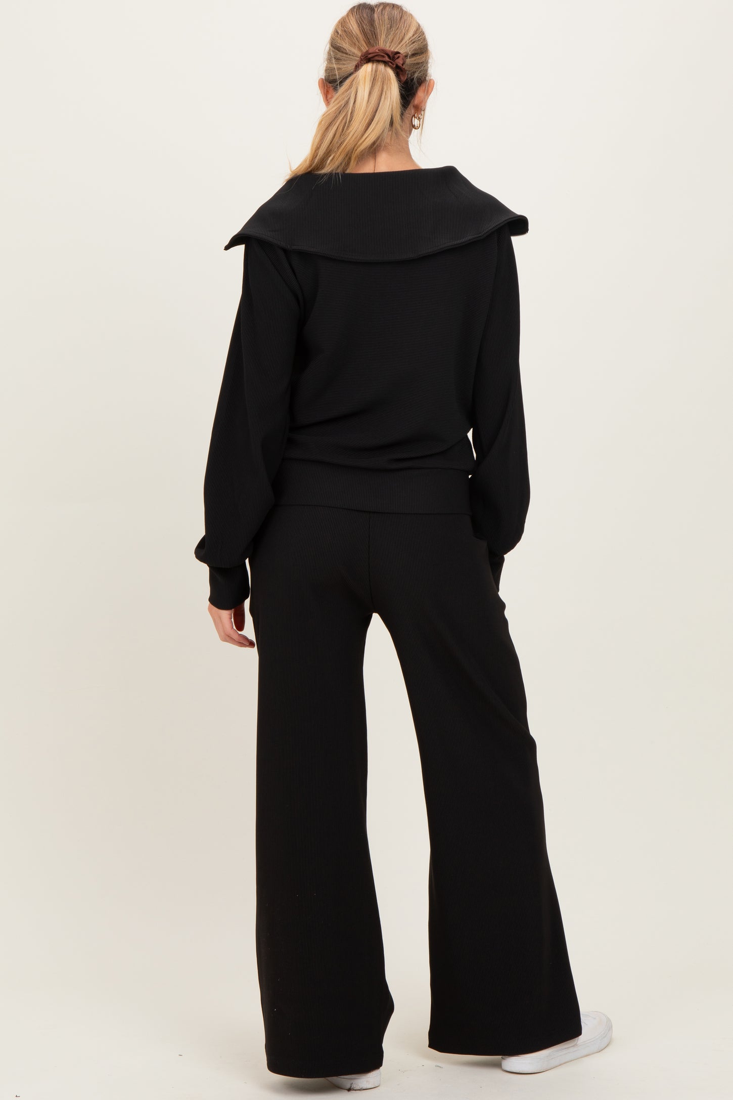 woman wearing a black maternity ribbed lounge set with a wide collar and flared pants, facing away from the camera