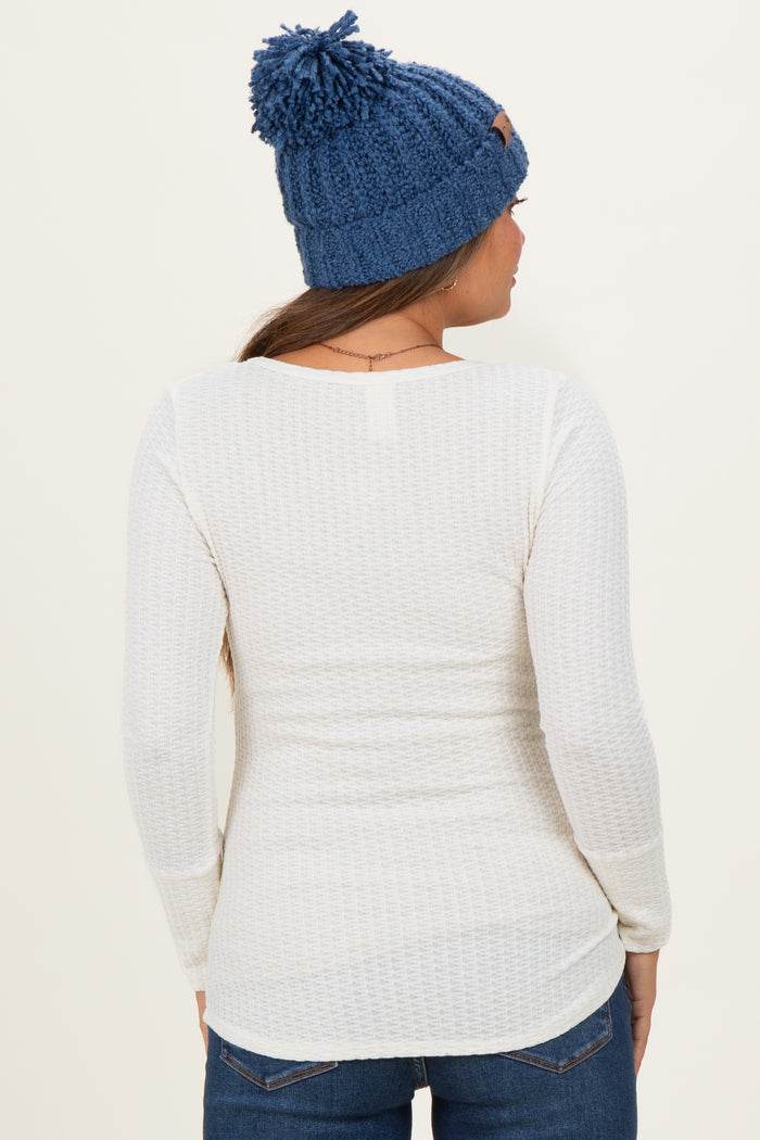 woman wearing a white long sleeve maternity top with a textured design and a blue knit beanie
