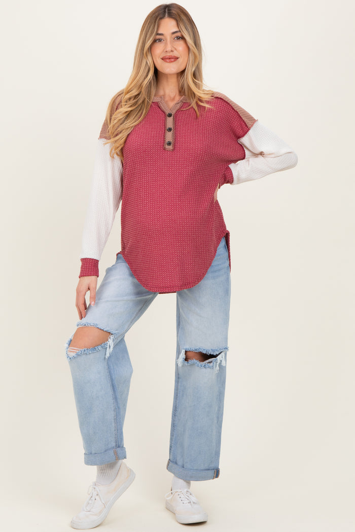 woman wearing a burgundy and white maternity top with a henley neckline and distressed light blue jeans, showing baby bump