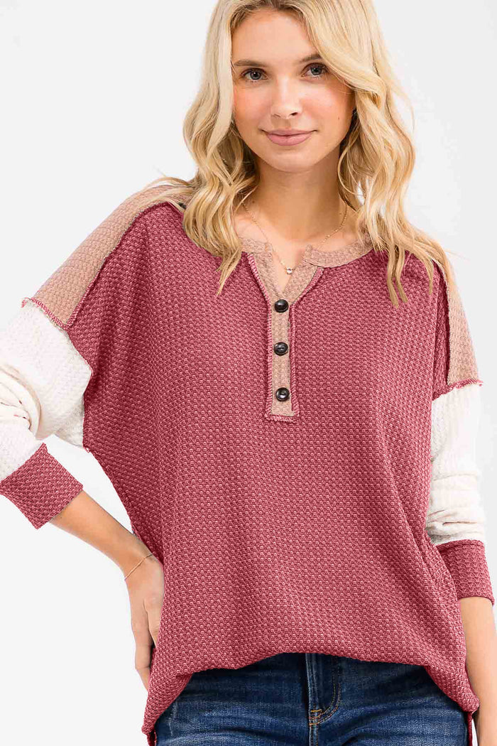 woman wearing a burgundy henley top with beige accents and button detail, styled with loose-fitting sleeves