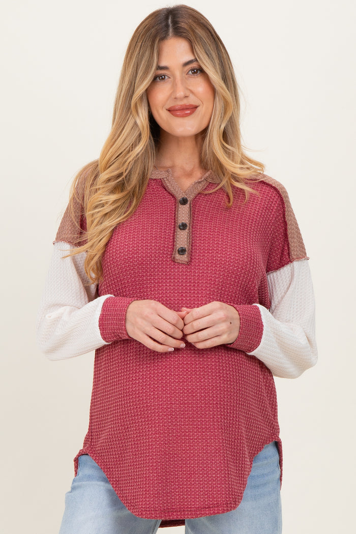 woman wearing a maroon and cream long sleeve maternity top with button details and a relaxed fit, showing her baby bump