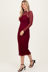 woman wearing a burgundy lace long sleeve midi dress with a fitted silhouette and side slit, paired with black heels