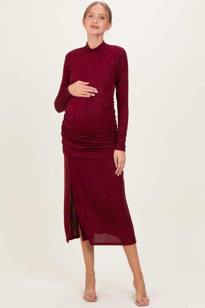 woman wearing a burgundy long sleeve maternity dress with ruched detailing and a side slit, showcasing her baby bump