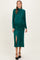 woman wearing a dark green maternity dress with long sleeves, ruched details, and a side slit