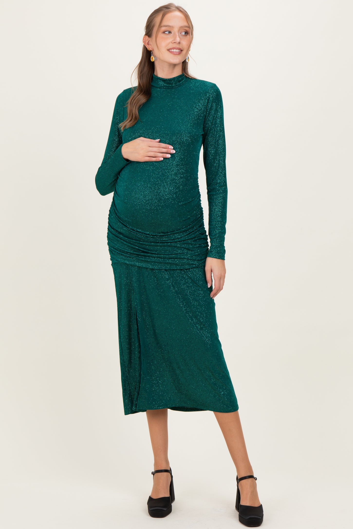 woman wearing a green sequined maternity dress with long sleeves and ruched details, holding her baby bump
