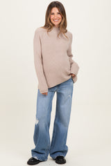 woman wearing a beige oversized ribbed maternity sweater and distressed wide-leg jeans, showing her baby bump