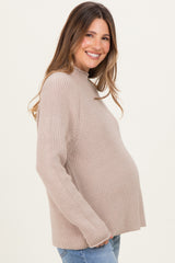 woman wearing a beige ribbed maternity sweater and showing her baby bump