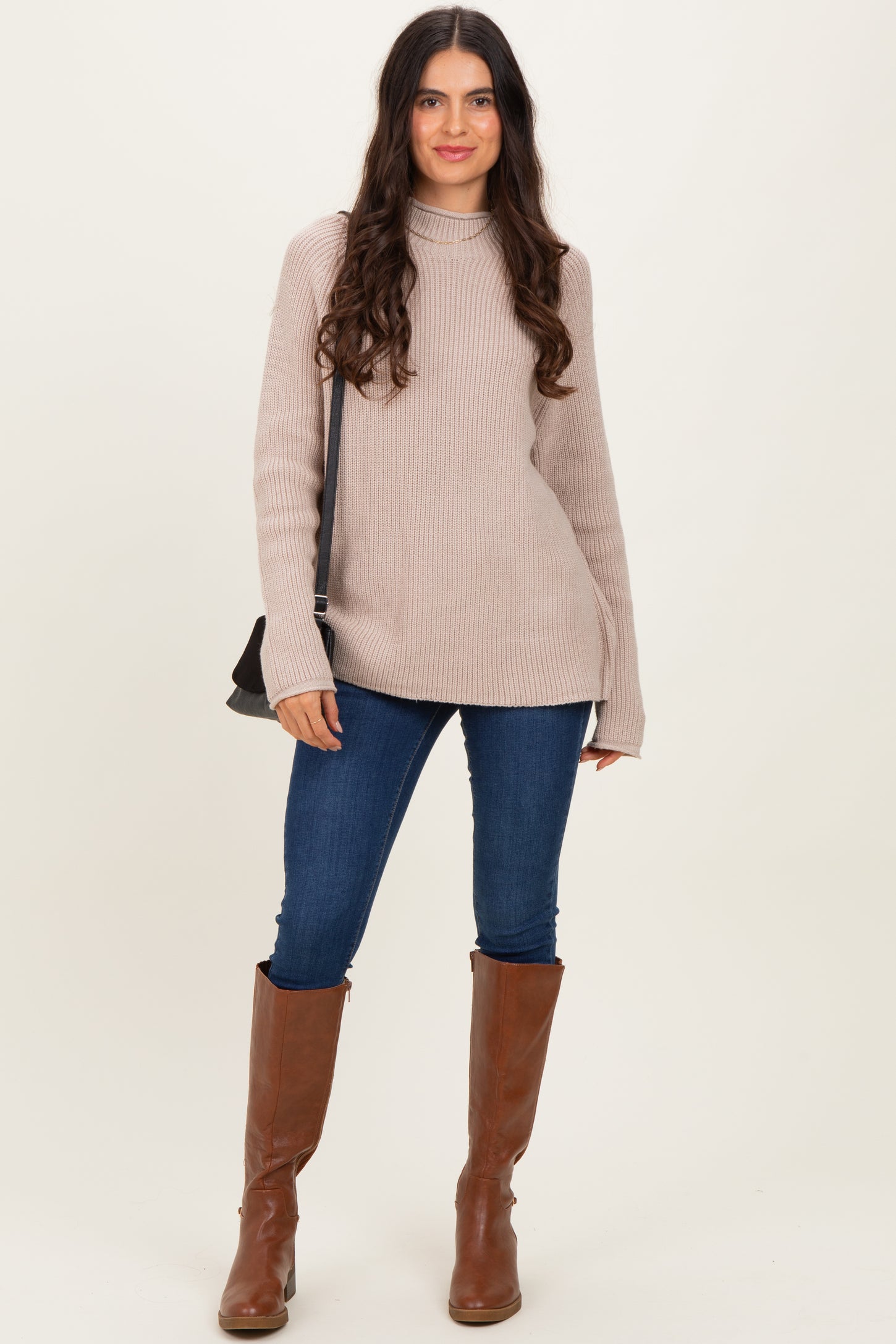 woman wearing a light beige ribbed knit sweater with a mock neck, paired with blue skinny jeans and brown knee-high boots