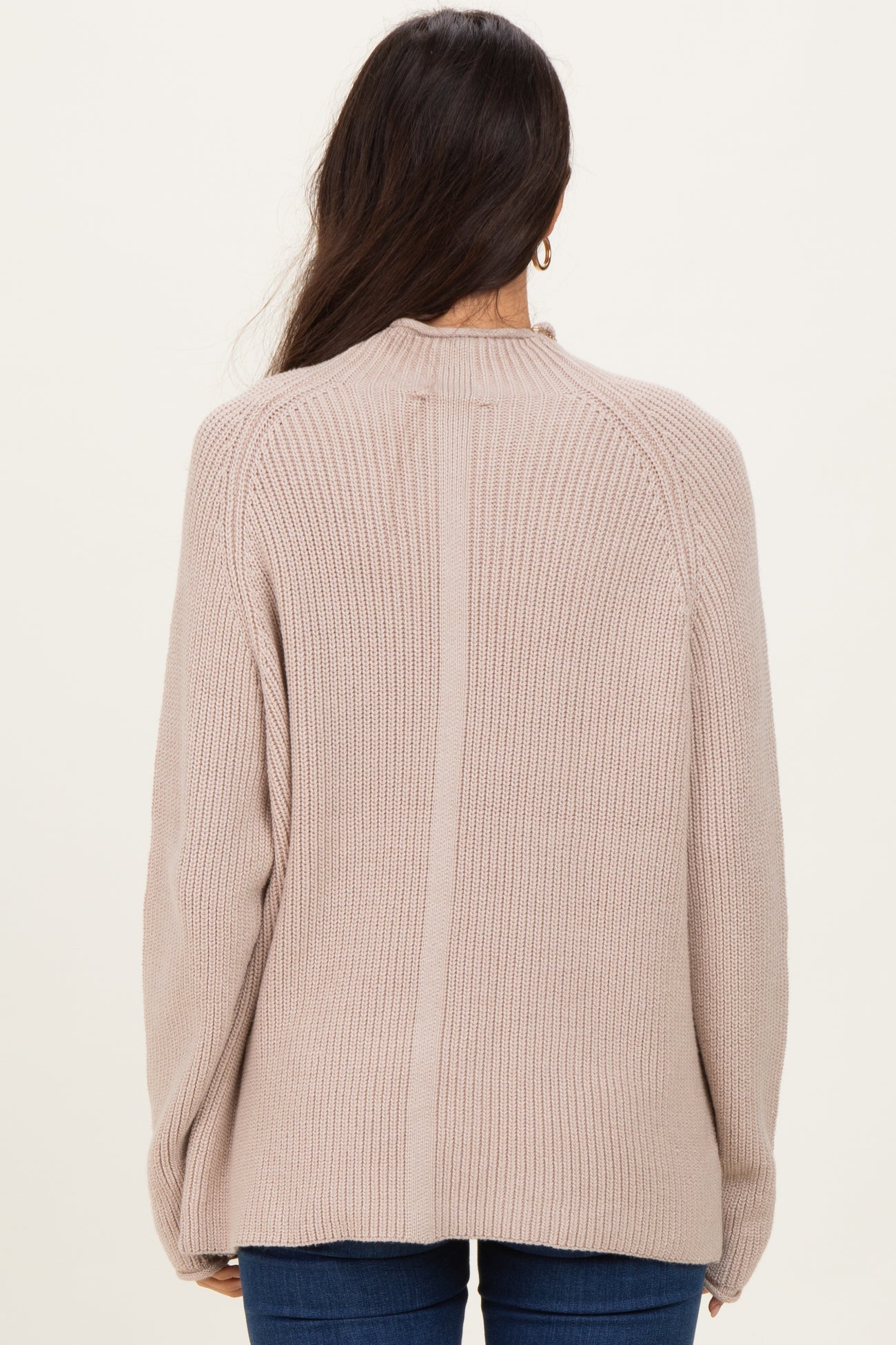 woman wearing a beige ribbed knit sweater, showing the back view and relaxed fit, paired with blue jeans