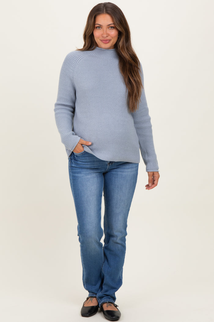 woman wearing a light blue maternity sweater and fitted jeans with a visible baby bump