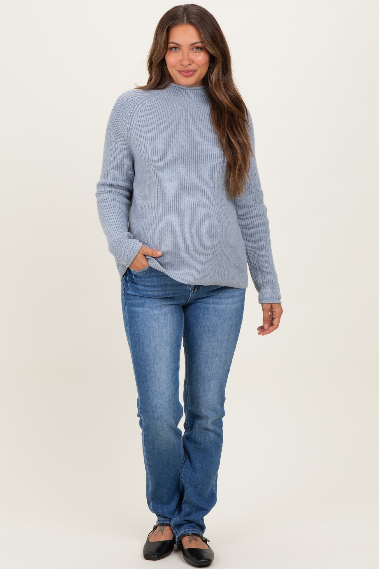 woman wearing a light blue maternity sweater and fitted jeans with a visible baby bump