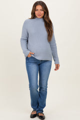 woman wearing a light blue maternity sweater and fitted jeans with a visible baby bump