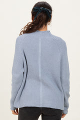 woman wearing a light blue ribbed sweater with a high neckline and long sleeves, viewed from the back