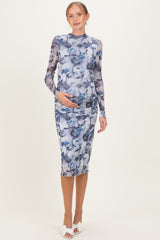 woman wearing a floral print long sleeve maternity dress, gently cradling her baby bump