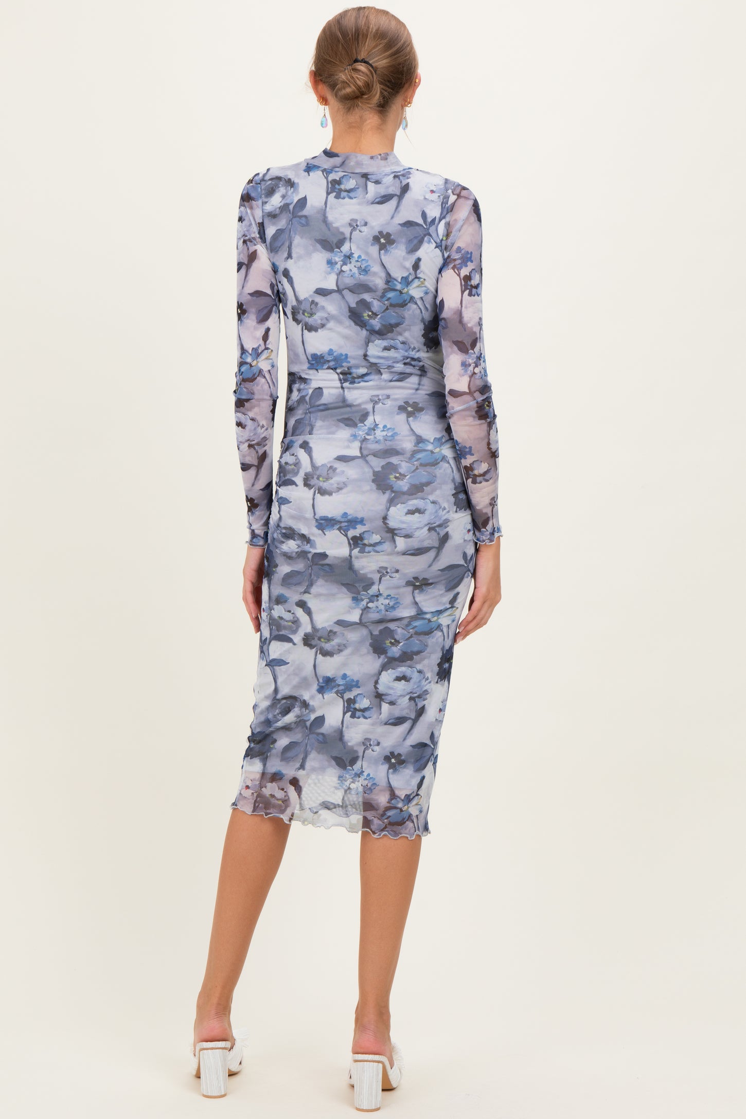 woman wearing a fitted long sleeve maternity dress in a floral blue print, showing a baby bump