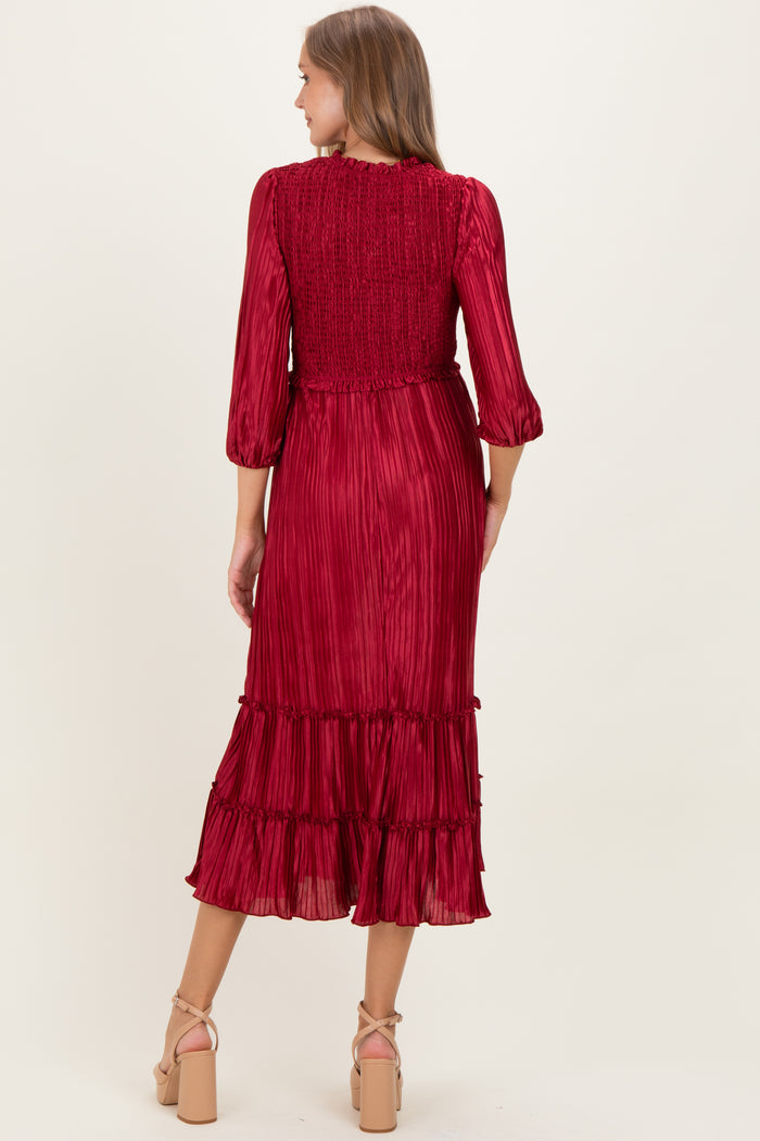 woman wearing a burgundy pleated maternity dress with three-quarter sleeves and a ruffled hemline