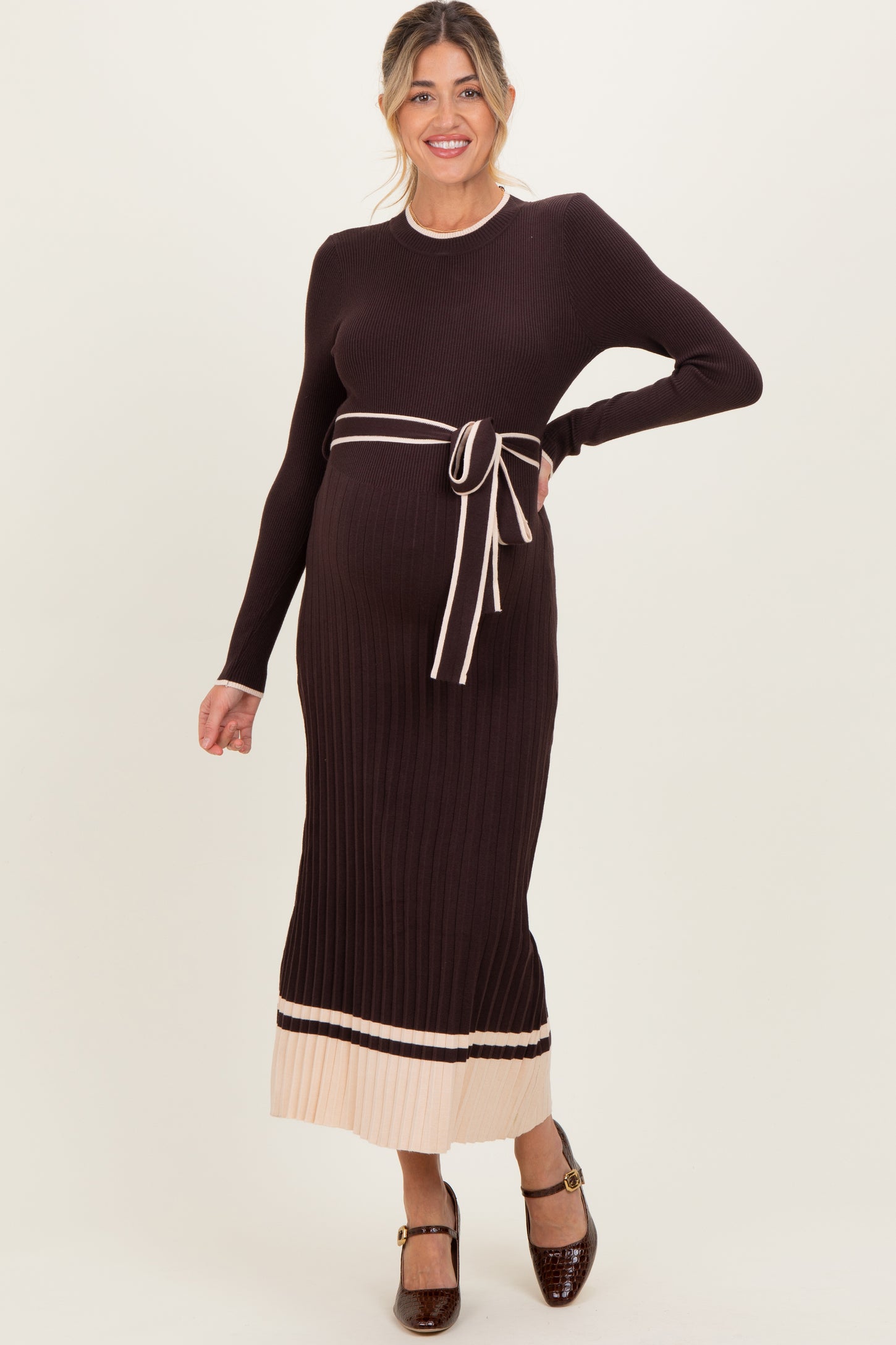 woman wearing a dark brown ribbed maternity sweater dress with a tie belt and light stripes at the hem, showcasing her baby bump