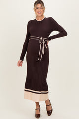 woman wearing a dark brown ribbed maternity sweater dress with a tie belt and light stripes at the hem, showcasing her baby bump