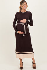 woman wearing a dark brown ribbed maternity dress with a tie waist and light beige hem, holding her baby bump