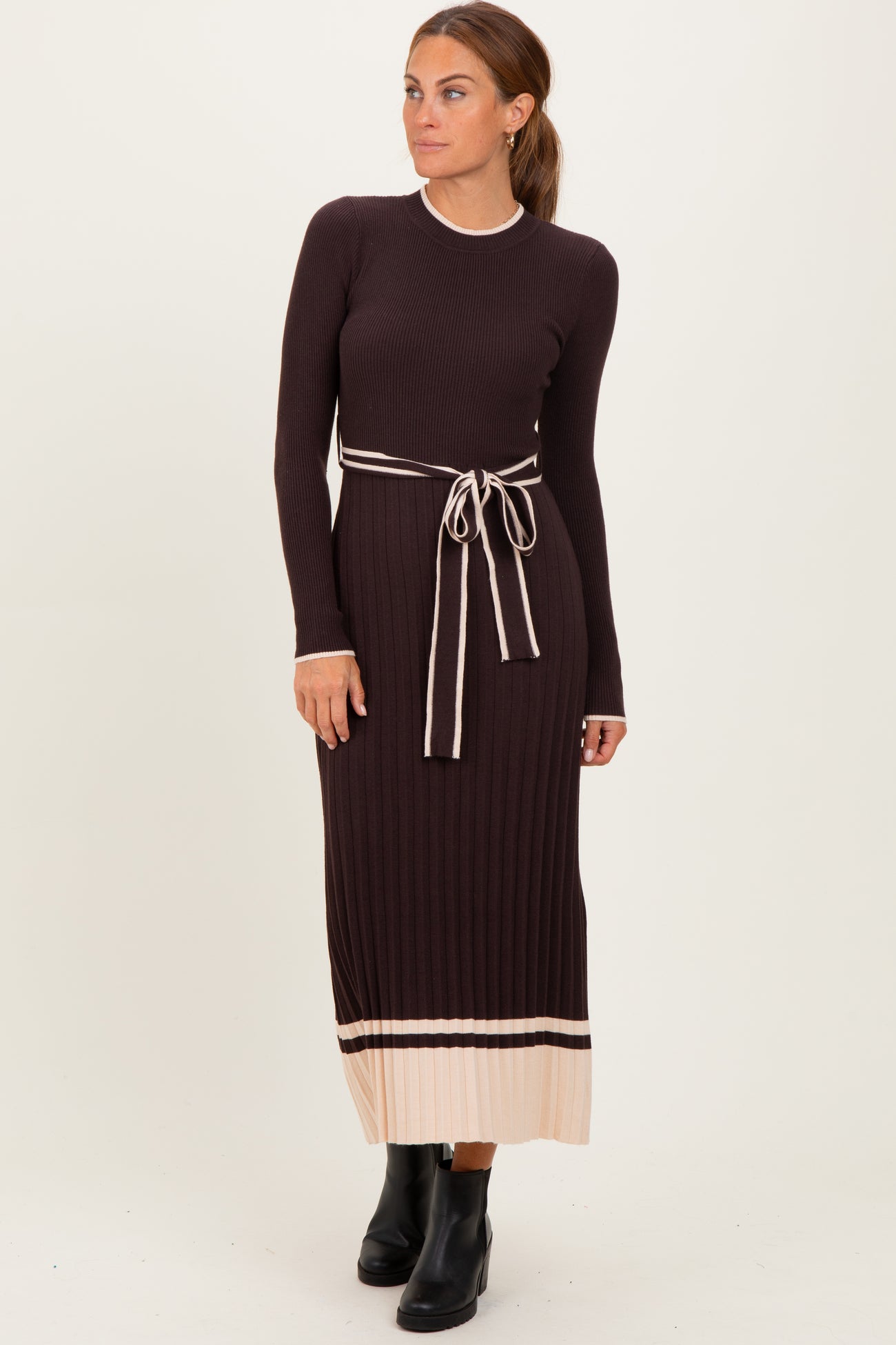 woman wearing a dark brown ribbed maxi dress with a tie belt and light beige accents, standing and looking to the side