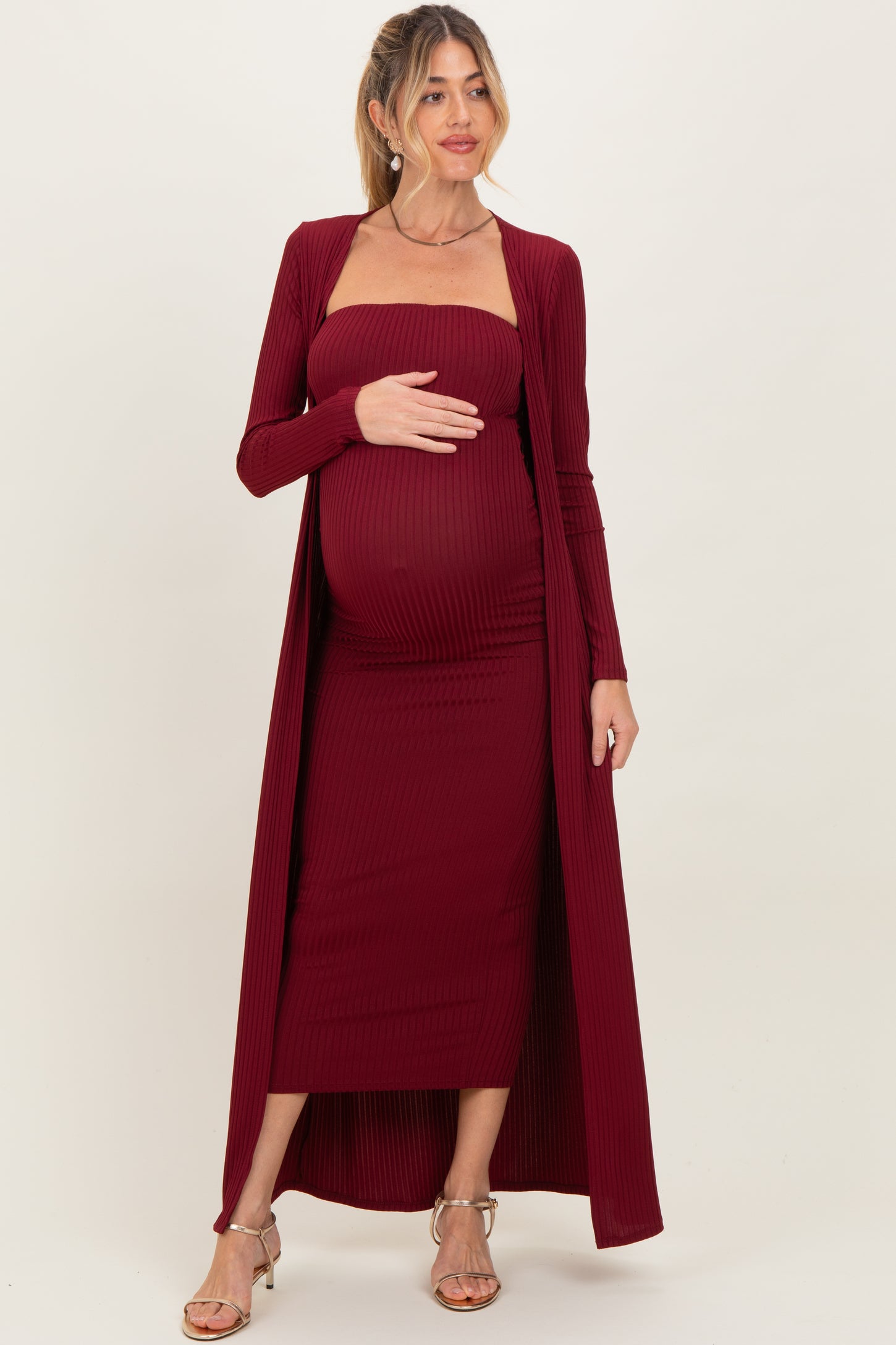 woman wearing a burgundy maternity ribbed dress with a long cardigan and holding her baby bump