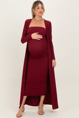 woman wearing a burgundy maternity ribbed dress with a long cardigan and holding her baby bump