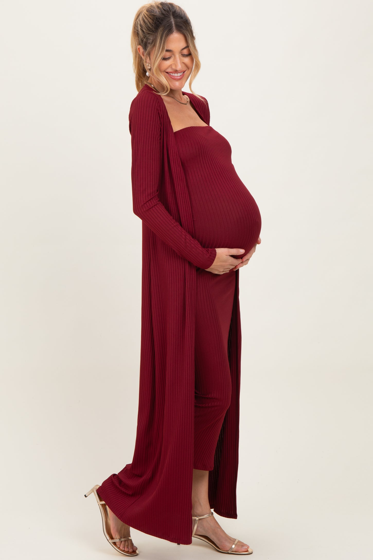 woman wearing a burgundy ribbed maternity set with a long cardigan and a fitted dress, showing her baby bump