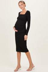 woman wearing a black long sleeve fitted maternity dress with ruching and holding her baby bump