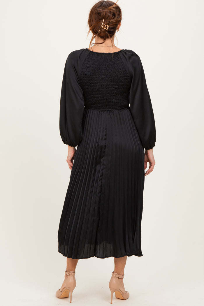 woman wearing a black pleated midi dress with long puff sleeves and a smocked bodice, view from the back