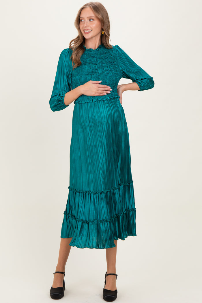 woman wearing a teal maternity dress with smocked bodice and tiered skirt, holding her baby bump