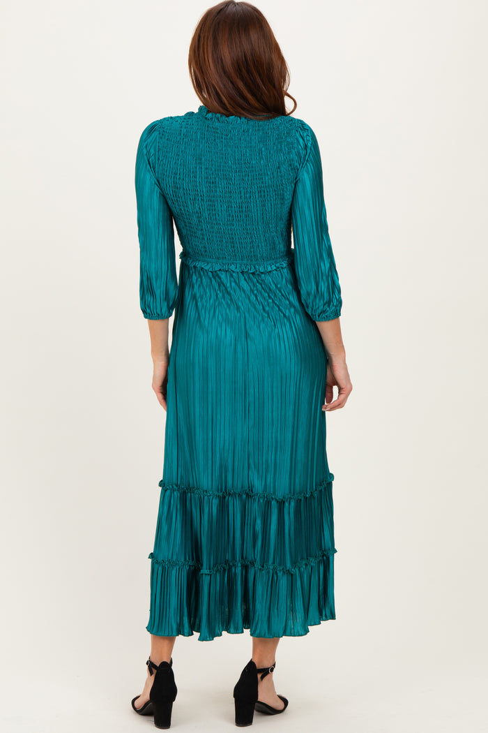 woman wearing a teal pleated long sleeve dress with a smocked bodice and tiered skirt