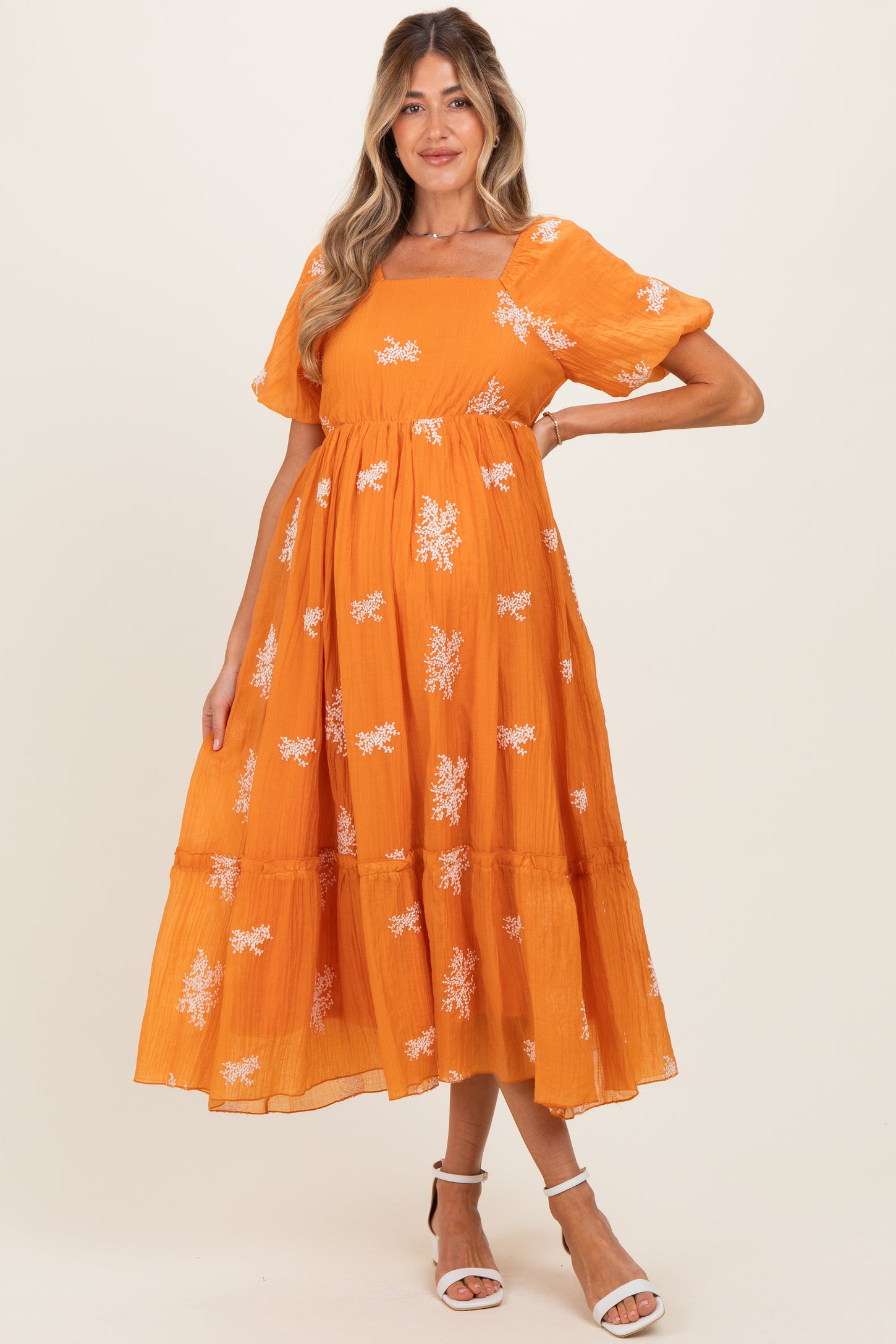 woman wearing an orange maternity dress with floral embroidery and puff sleeves, showcasing her baby bump