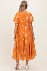 woman wearing an orange floral embroidered maternity dress with short sleeves and a tiered skirt, showing her baby bump from behind