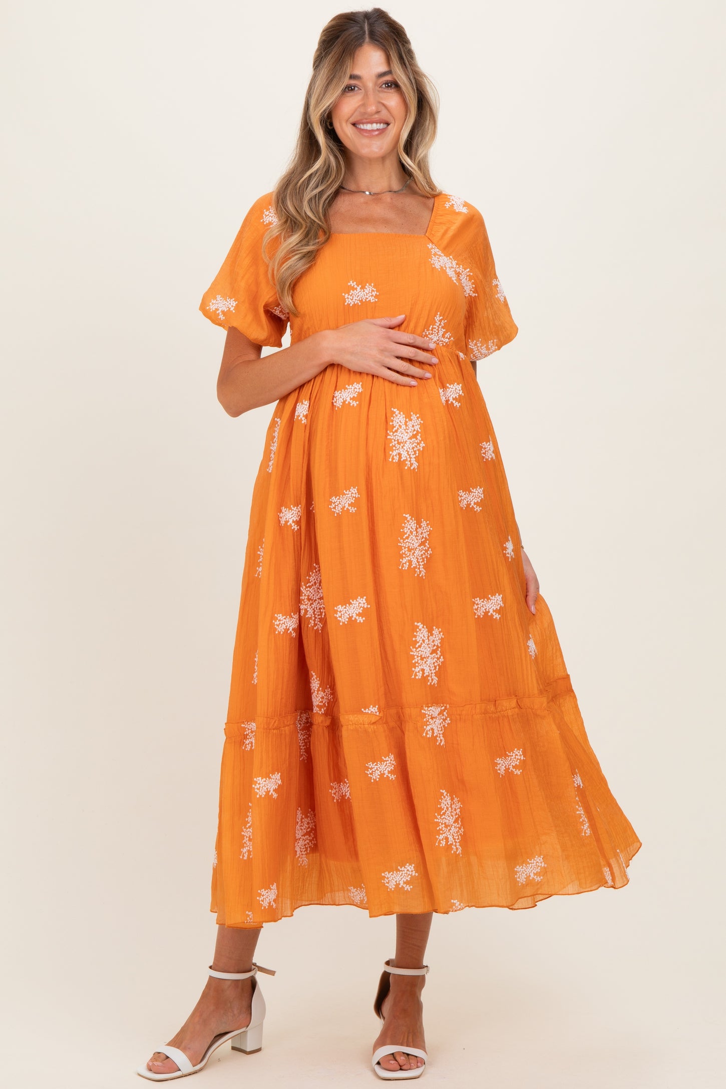 woman wearing an orange maternity dress with floral embroidery and short sleeves, holding her baby bump