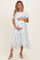 woman wearing a light blue maternity dress with embroidered floral details and short puff sleeves, holding her baby bump