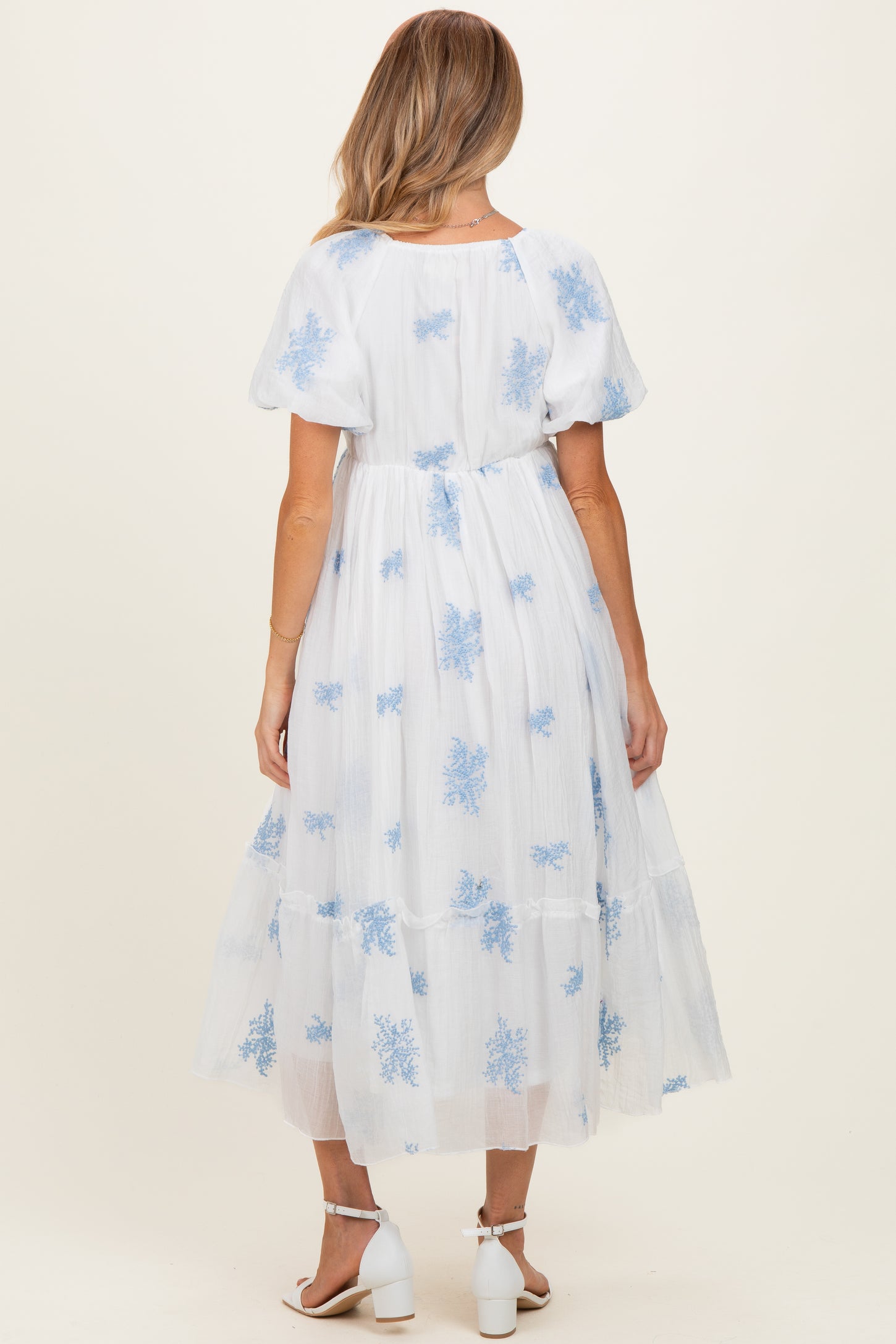 woman wearing a white maternity dress with blue floral embroidery and puff sleeves, showcasing a flowy maxi style