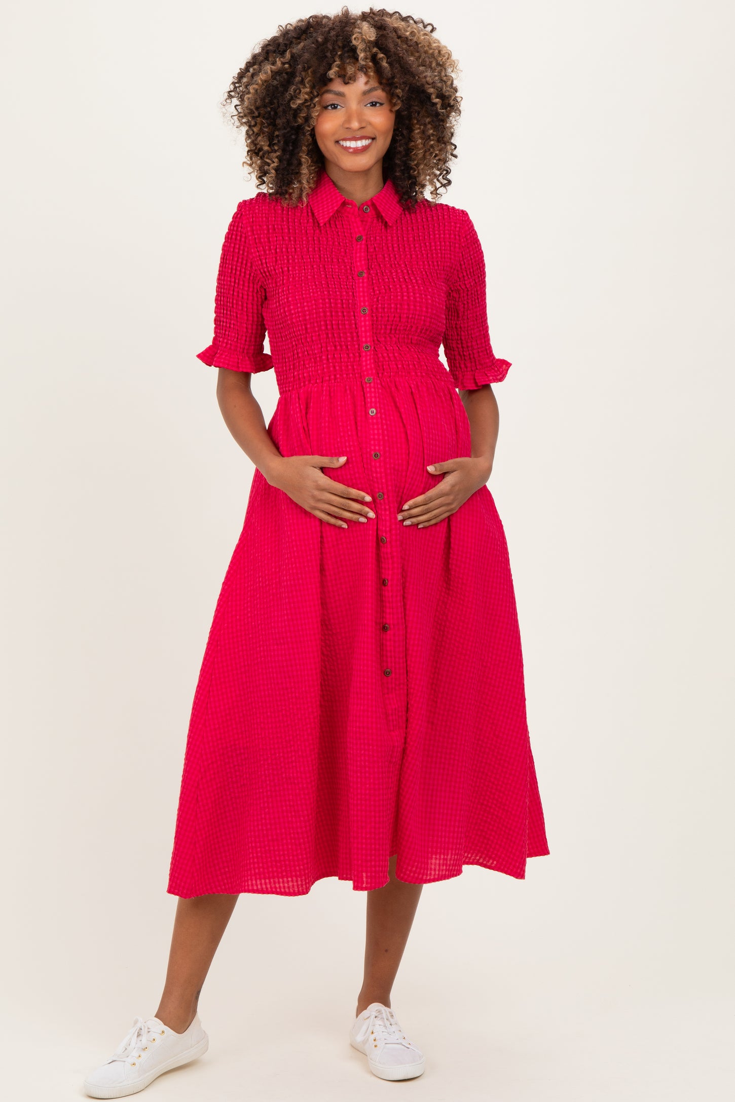 woman wearing a bright pink maternity dress with a button-down front and a belted waist, showing her baby bump