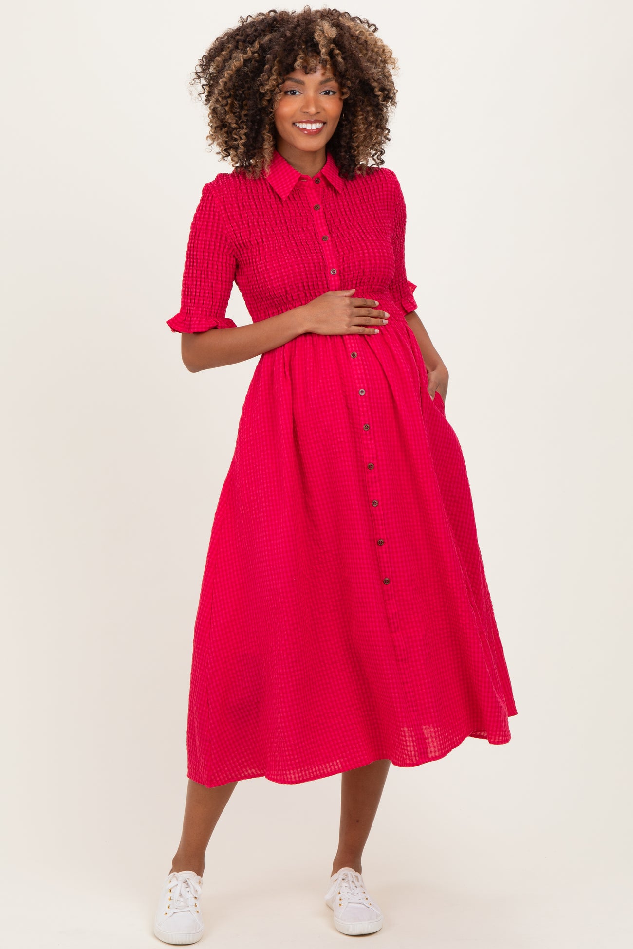 woman wearing a bright pink short sleeve maternity dress with buttons and holding her baby bump