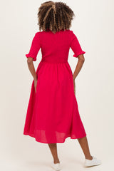 woman wearing a bright pink maternity dress with a smocked bodice and short sleeves, shown from the back