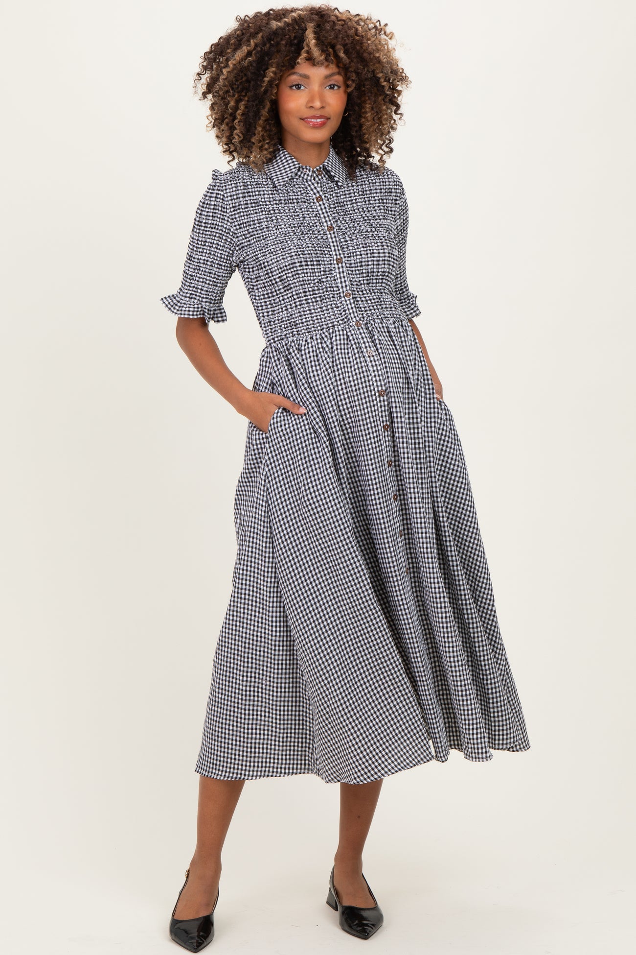 woman wearing a black and white gingham maternity dress with a smocked waist and pockets, displaying a baby bump