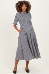 woman wearing a black and white gingham maternity dress with a smocked waist and pockets, displaying a baby bump