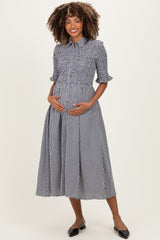 woman wearing a black and white checkered maternity dress with puff sleeves and a smocked bodice, holding her baby bump