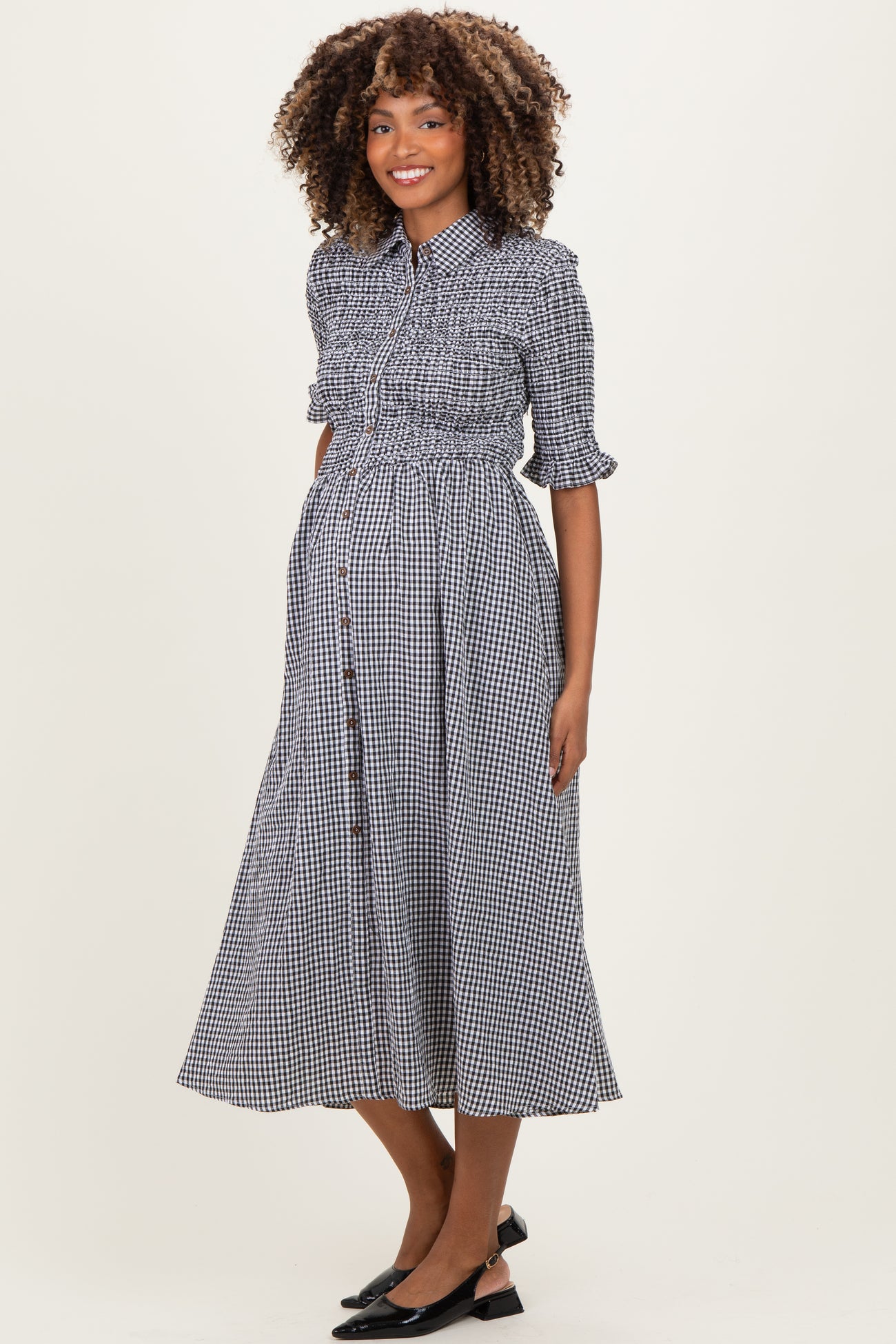 woman wearing a black and white checked maternity dress with puff sleeves and a button-down front, showing her baby bump